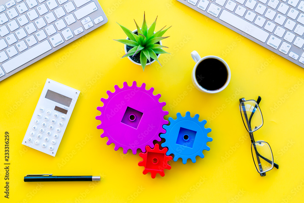 Aufkleber teamwork in business concept. toy gears on yellow office desk with computer keyboard top view