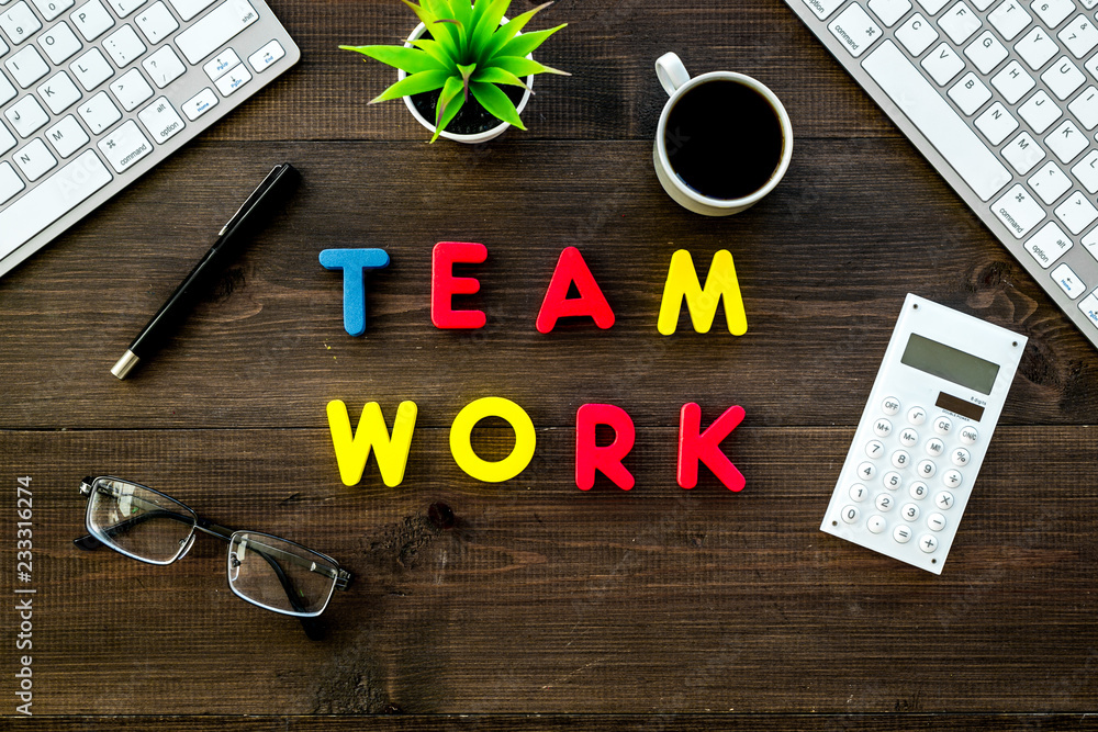 Aufkleber teamwork in office. text teamwork lined with colored letters on dark wooden office desk with compute