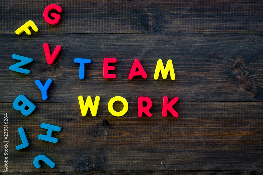 Poster teamwork training concept. text teamwork lined with colored letters near toy letters on dark wooden 