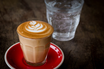 Piccolo Latte art in small glass with red ceramic plate topping beautiful flower art from milk