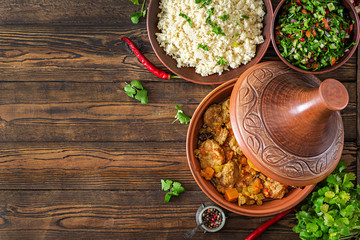 Traditional tajine dishes, couscous  and fresh salad  on rustic wooden table. Tagine lamb meat and...