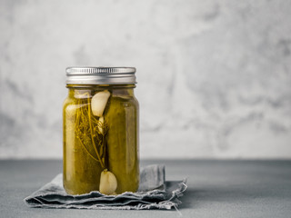 Glass jar with pickled cucumbers on gray background with copy space for text. Perfect homemade...