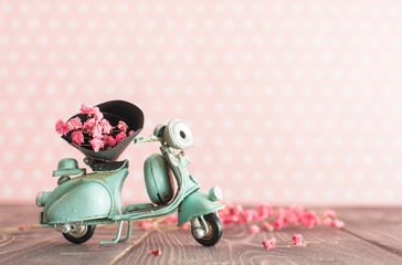 Vintage toy blue mototrcycle with bunch of pink flowers on wooden table