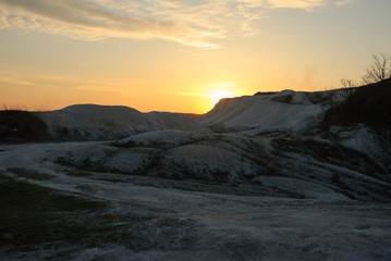 A blue sunset sky with white clouds and white Cretaceous deposits. Extraction of chalk. An open chalk rock quarry mine. Industrial extraction of chalk and clay by mining. Sunset lighting.