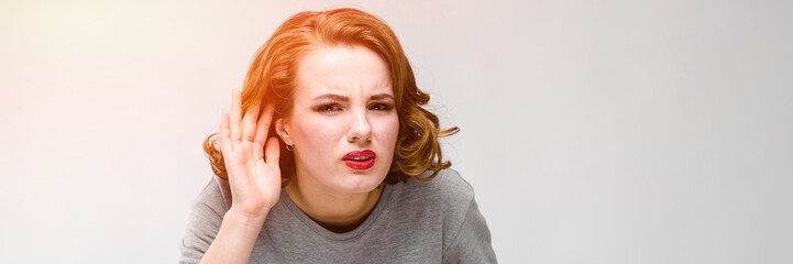 Charming young girl in a gray T-shirt on a gray background. The girl put her hand to her ear