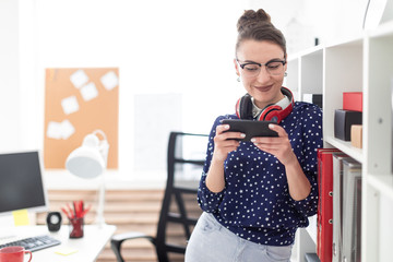 A young girl in glasses stands in the office on the floor of the rack and holds a phone in her...