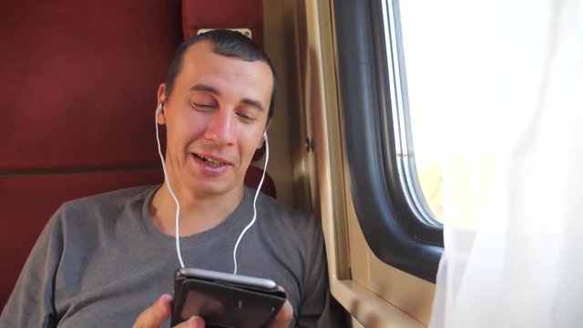 man listening to the music on the train rail car coupe lifestyle compartment travel. slow motion video. man with a smartphone at the window of a train in a car travel internet social media web. man