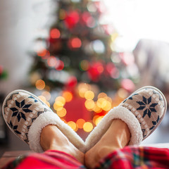 Legs in slippers on Christmas tree background