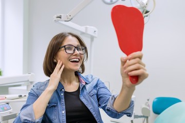 Woman patient looking in the mirror at the teeth, sitting in the dental chair. Healthcare, medical and dentistry concept