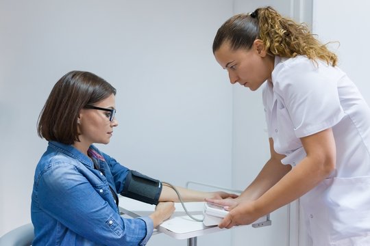 Nurse Taking Female Patient's Blood Pressure In Office