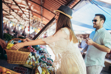 Young couple buying fruits and vegetables in a market on a sunny morning.