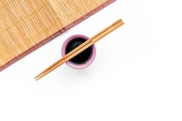 Chinese meal concept. soy sauce in bowl near chopsticks and bamboo table mat on white background...
