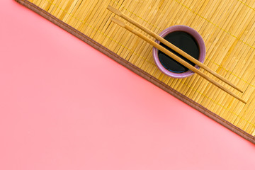 Chinese meal concept. soy sauce in bowl near chopsticks and bamboo table mat on pink background top...