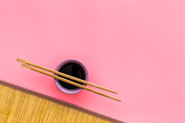 Chinese meal concept. soy sauce in bowl near chopsticks and bamboo table mat on pink background top...
