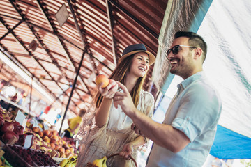 Young couple buying fruits and vegetables in a market on a sunny morning.