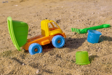 Yellow toy dumper truck in sand on the beach with green tipper trailer and blue wheels