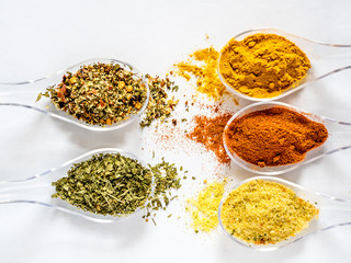 Various spices selection on spoon lined up, face to face on a white background. Assortment of powder spices on spoons isolated on a white background.