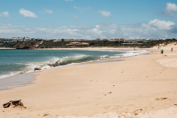 Fototapeta na wymiar Waves at the beach off the coast of Portugal. Atlantic Ocean. People rest on the beach.