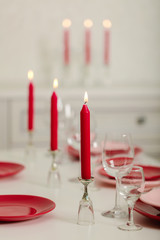 Merry Christmas and Happy New Year! Table setting - red and pink dishes, holiday knitted decor - Santa Claus knitted hats on the bottle with wine, red candles.