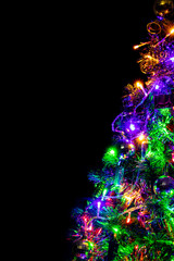 Colored decoration of Christmas tree on dark background. Part of X-mas tree with lighting bulb and decoration at night.