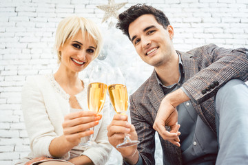 Couple clinking with sparkling wine for Christmas sitting in front of white tree