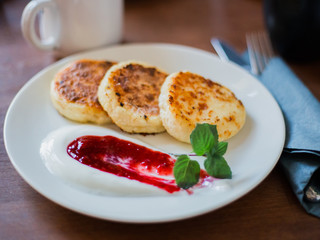 sweet cheese pancakes with sour cream on a white plate