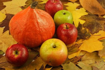 Naklejka na ściany i meble Orange pumpkin and apples placed on the dry autumn leaves, background