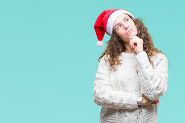 Young brunette girl wearing christmas hat over isolated background with hand on chin thinking about question, pensive expression. Smiling with thoughtful face. Doubt concept.