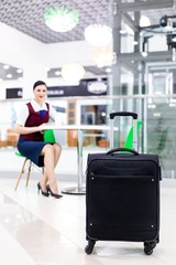 Fototapeta na wymiar Stewardess with red lips sitting in the waiting room, in the foreground is a suitcase