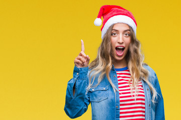 Beautiful young blonde woman wearing christmas hat over isolated background pointing finger up with successful idea. Exited and happy. Number one.