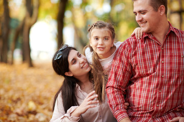 Fototapeta premium Happy family is in autumn city park. Children and parents. They posing, smiling, playing and having fun. Bright yellow trees.