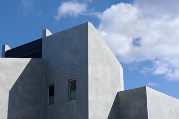 Architectural detail of a modern concrete residential building against a cloudy blue sky.