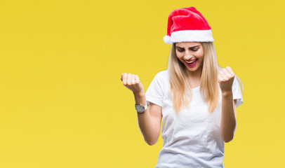 Fototapeta na wymiar Young beautiful blonde woman christmas hat over isolated background very happy and excited doing winner gesture with arms raised, smiling and screaming for success. Celebration concept.