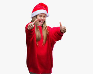 Young beautiful girl wearing christmas hat over isolated background approving doing positive gesture with hand, thumbs up smiling and happy for success. Looking at the camera, winner gesture.