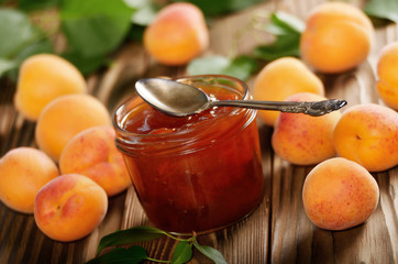 Glass Jar of Apricot jam on wooden table with ripe apricots at background