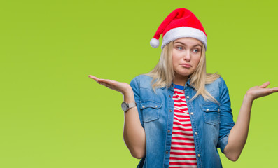 Young caucasian woman wearing christmas hat over isolated background clueless and confused expression with arms and hands raised. Doubt concept.