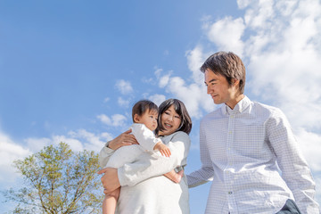 青空の下で赤ちゃんを抱く妊娠後期の幸せな女性と夫。育児、妊娠、家族、親子、愛、幸せイメージ