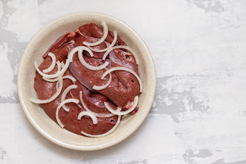 raw liver with onion in dish on white ceramic background