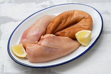 raw chicken breast with smoked sausage and lemon on dish