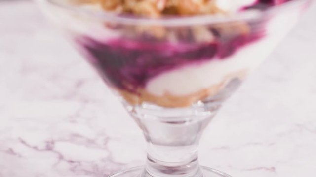 Figs pudding parfait with yogurt, blueberry jam, figs, hazelnut, and cookies in glass on white marble background. Flatlay top view.