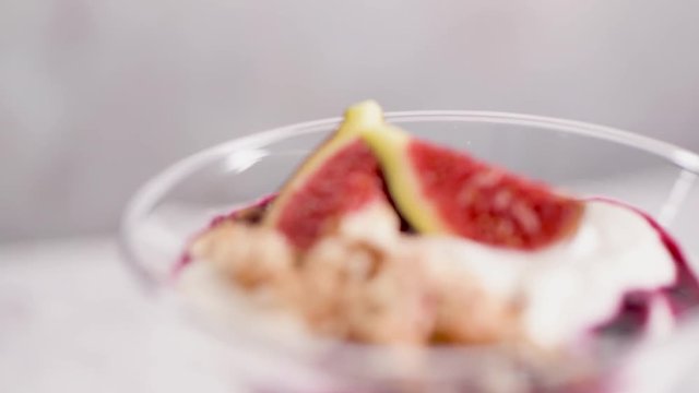 Figs pudding parfait with yogurt, blueberry jam, figs, hazelnut, and cookies in glass on white marble background. Flatlay top view.