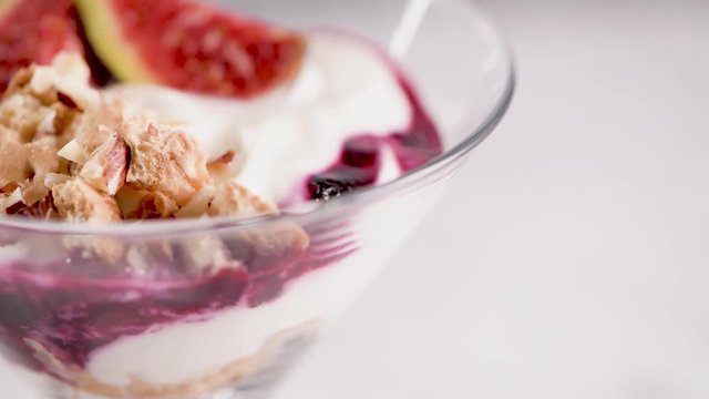 Figs pudding parfait with yogurt, blueberry jam, figs, hazelnut, and cookies in glass on white marble background. Flatlay top view.