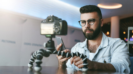 Bearded male video blogger creates video content for his channel. Man vlogger relieves himself on camera with tripod.