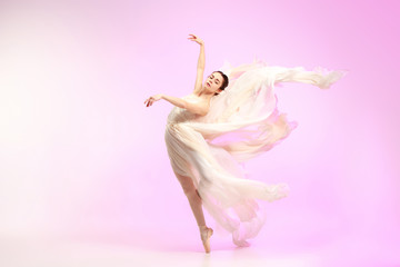 Young graceful female ballet dancer or classic ballerina dancing at pink studio. Caucasian model on...