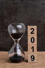 New year 2019 time countdown or business goals concept, hourglass or sandglass and stack of cube wooden block building number 2019 on wood table with dark blackboard background