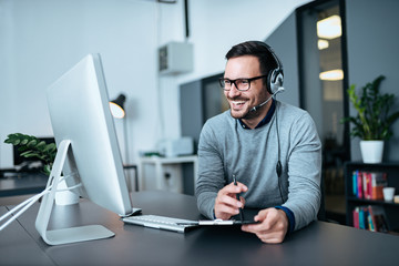 Portrait of a casual smiling businessman using headset when talking to customer.