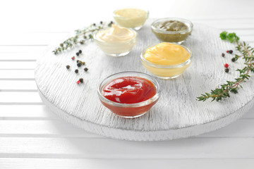 Different tasty sauces in bowls on white wooden board