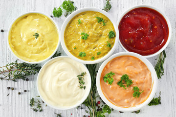 Different tasty sauces in bowls with spices on white wooden table