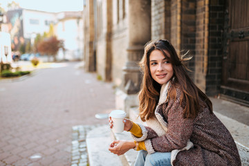 Beautiful stylish woman sitting on street stairs with takeaway coffee.