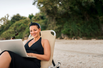 Freelance work concept. Close-up of young woman sitting on the beach with laptop. Copy space.